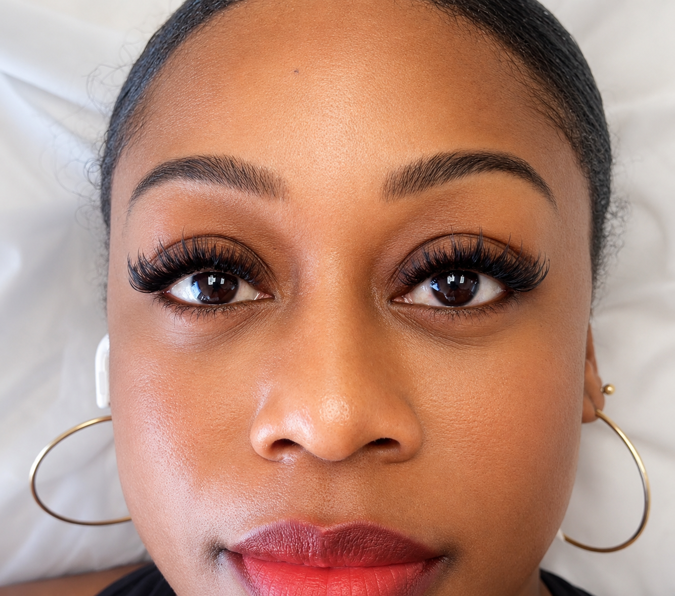 Client with full volume lash extensions, gold hoop earrings and red lipstick