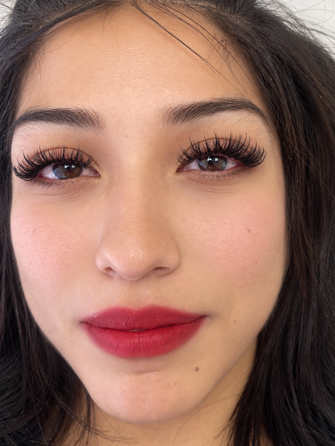 Client smiling with bold lash extensions and red lipstick